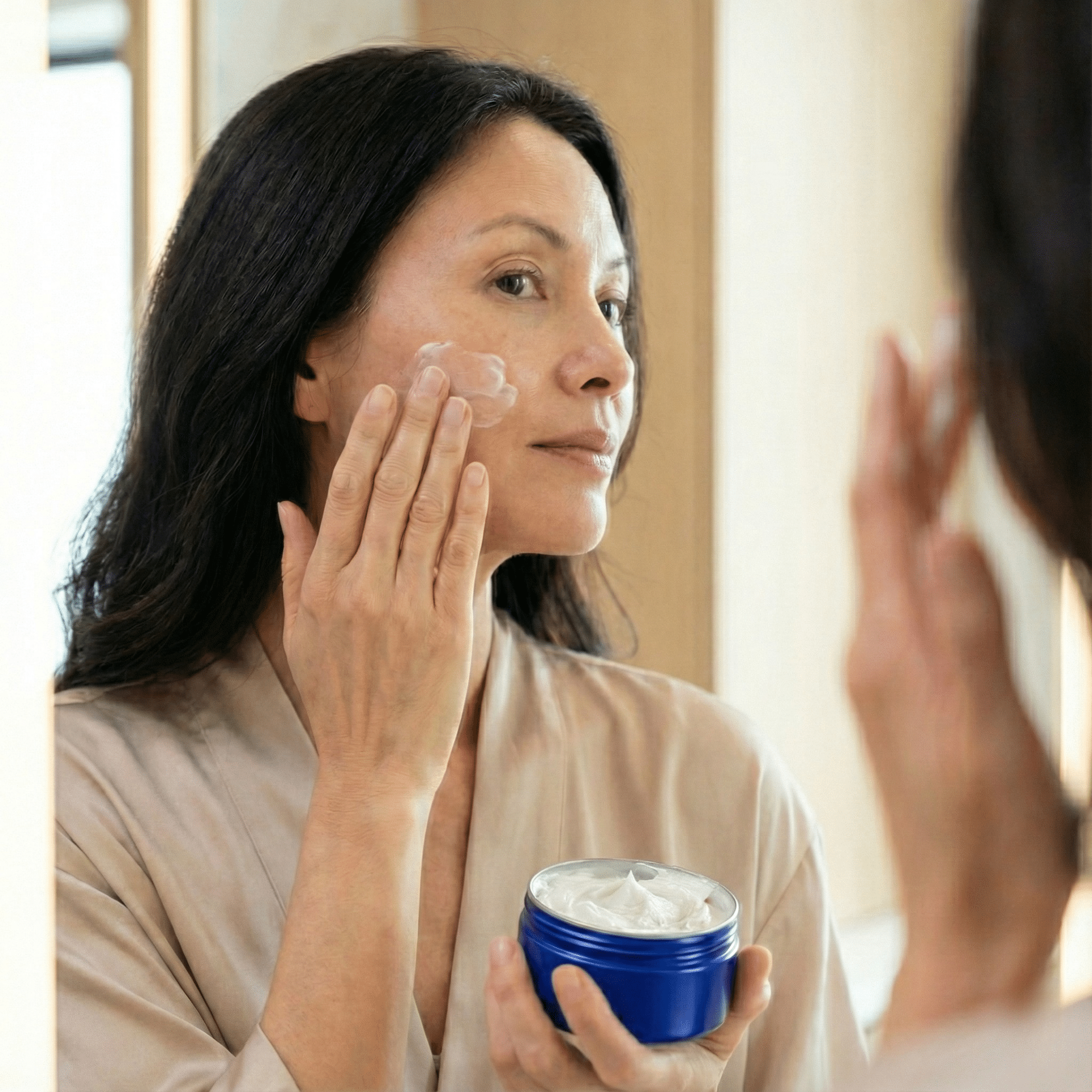 Mujer aplicando crema facial frente al espejo, utilizada en un artículo de un centro de estética ecológica en Barcelona sobre el uso de cosmética convencional.